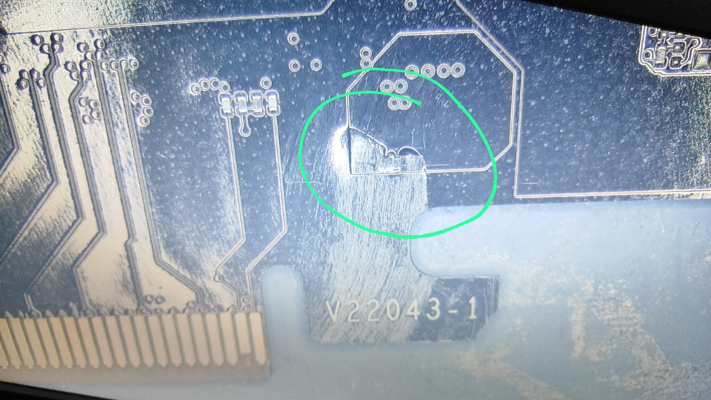 Close-up of a printed circuit board (PCB) showing visible damage near the PCIe connector, highlighted with a green circle.